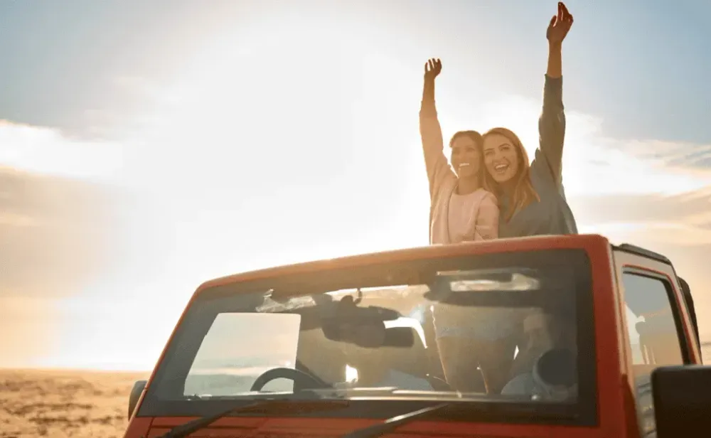 Couple With Friends On Vacation Driving Car On Road Trip Adventure To Beach Standing Up Through Roof